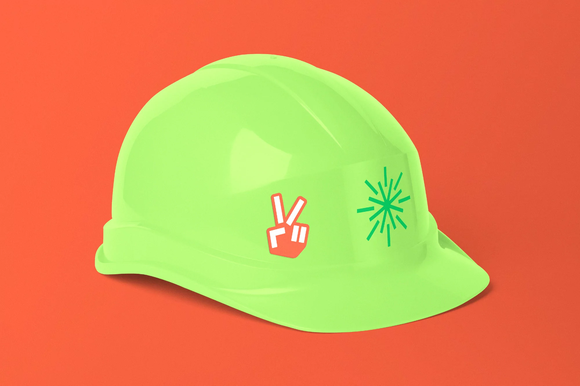 Bright neon green construction hat with peace sign and starburst stickers on a vivid orange background with subtle shadows.