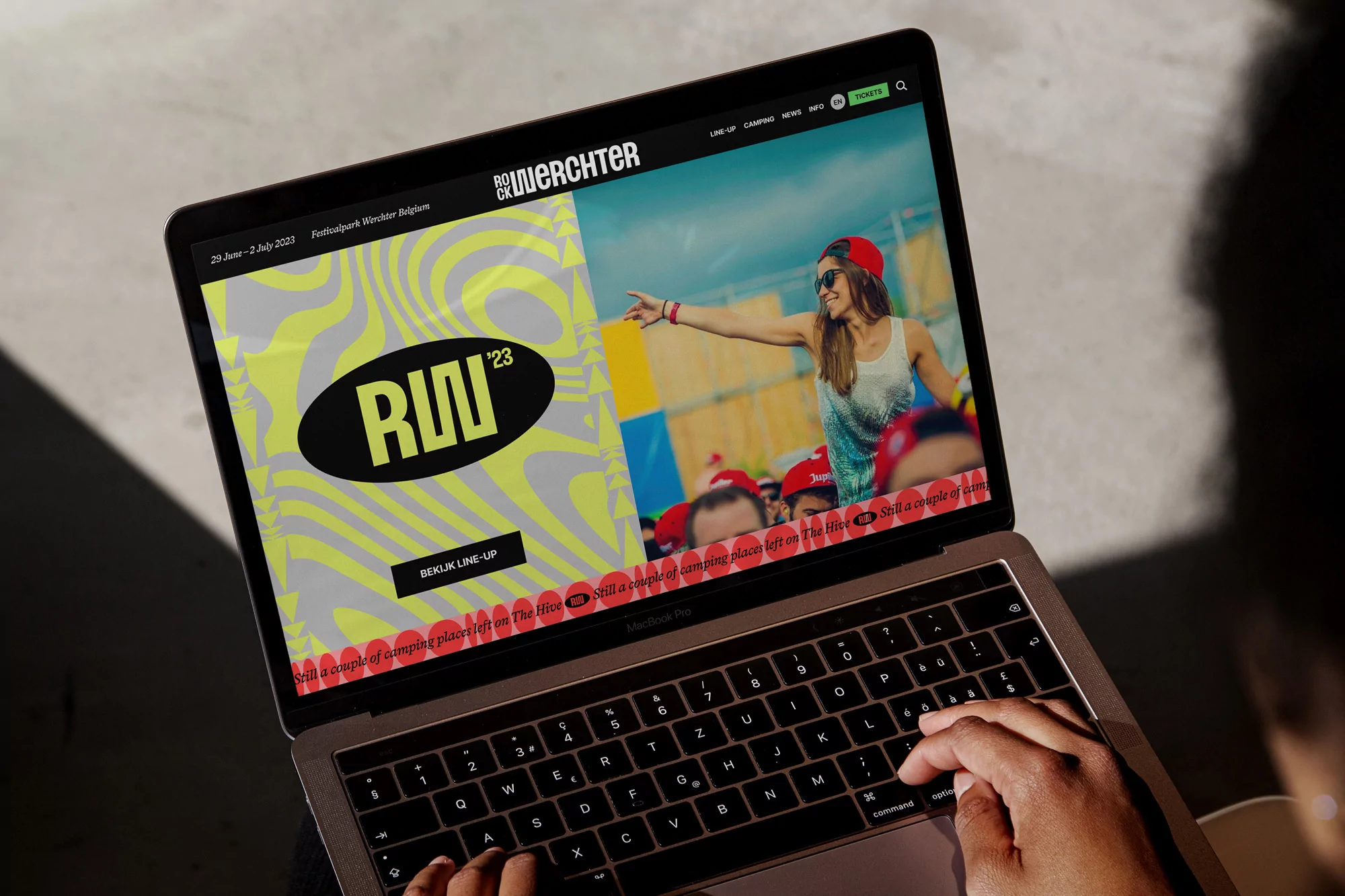 View of the Rock Werchter music festival webpage open on a laptop, showing people at the festival and the event logo. Focus on laptop screen.