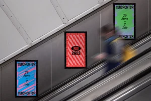 Rock Werchter 2023 festival posters displayed on a metallic station wall beside a blurred commuter on an escalator