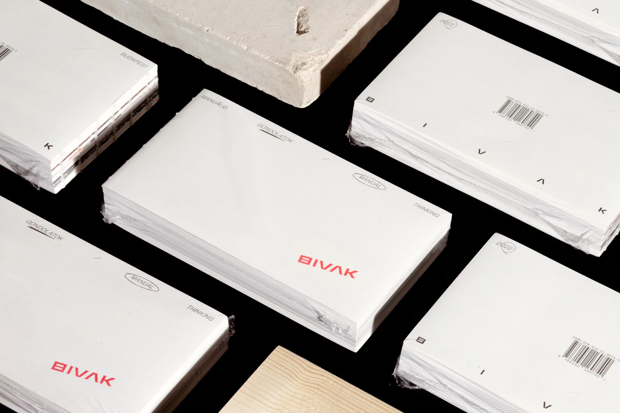 Stacks of white booklets with red text feature a minimalist design aesthetic against a black background, showcasing a modern presentation.