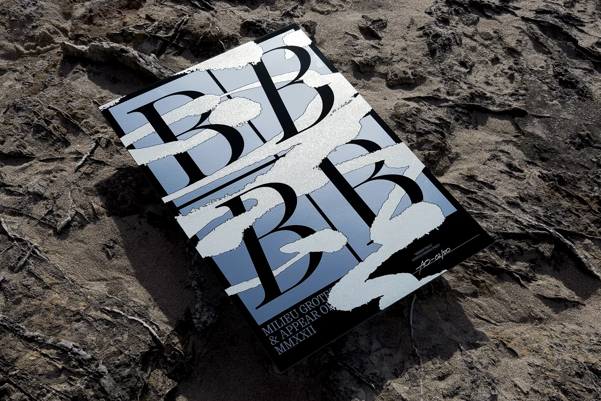 Close-up of a black and light blue colored poster with bold stylized text lying on a rough textured stone surface outdoors.