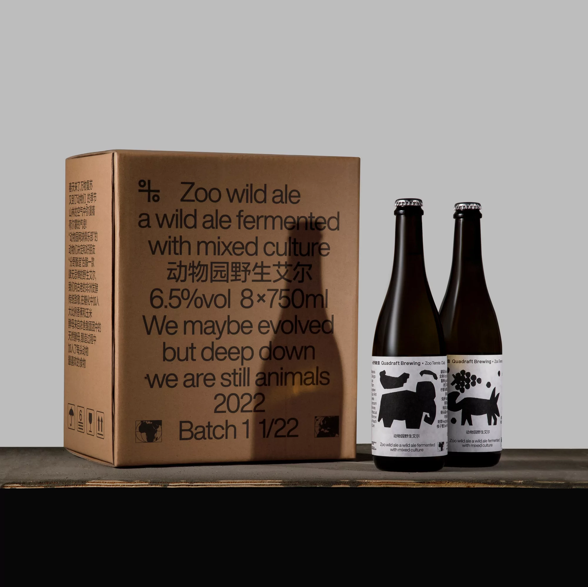 Two bottles of Zoo Wild Ale next to a cardboard box with product information, on a dark wooden surface against a neutral background.