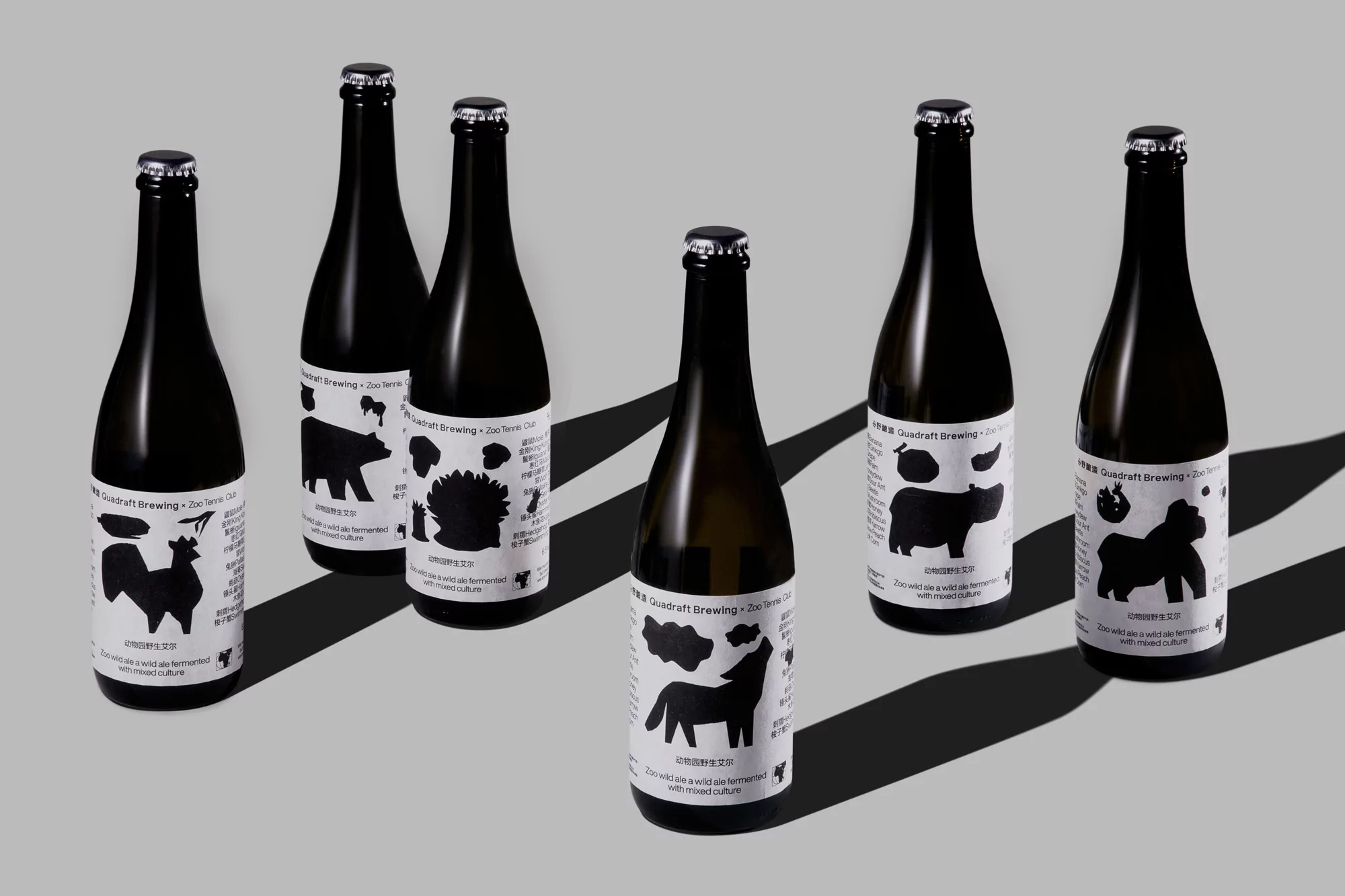 Seven black bottles of Quadraft Brewing beer with animal label art, set on a gray background with natural shadows.