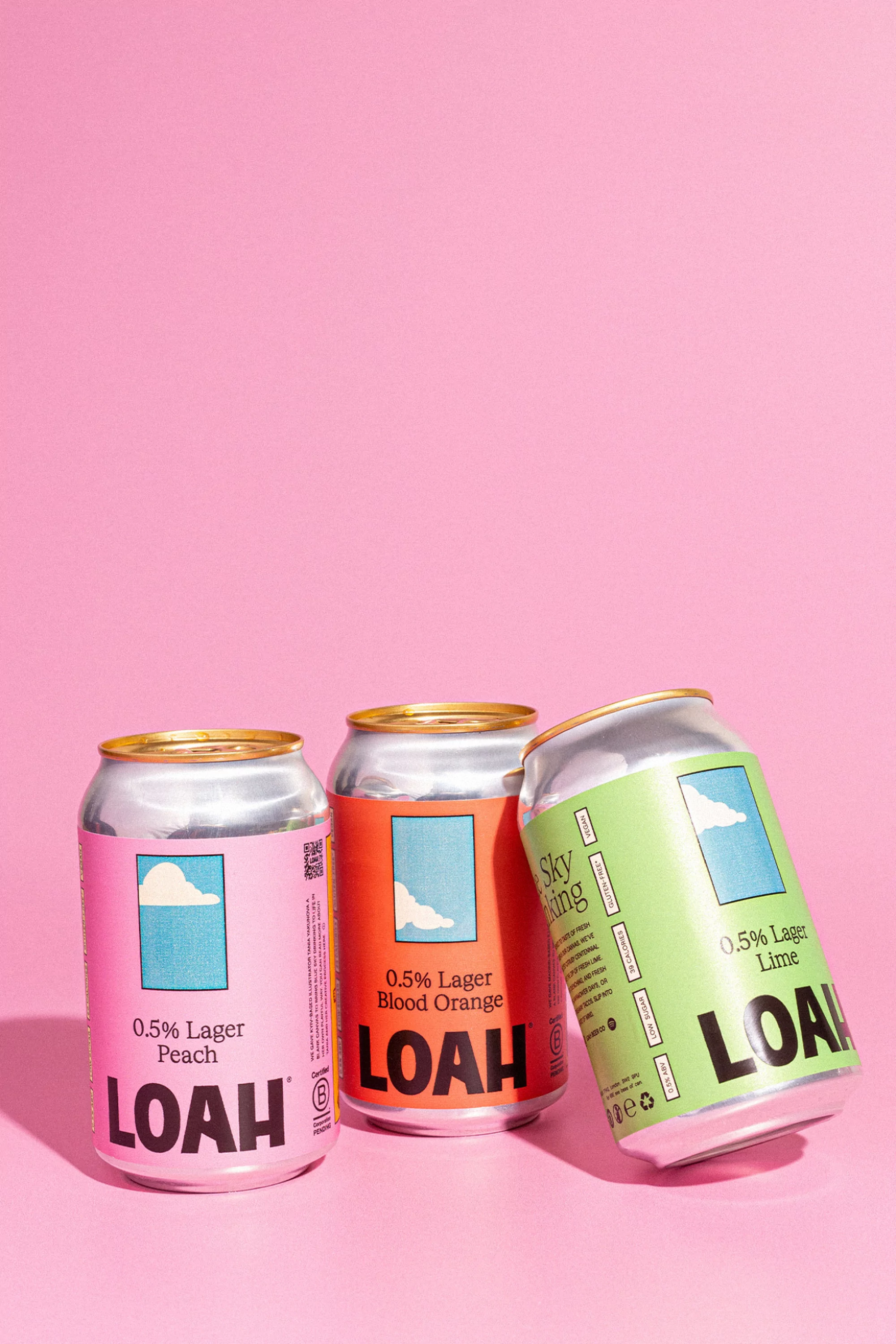 Three colorful LOAH lager cans: peach, blood orange, and lime flavors. These are displayed against a vibrant pink background.