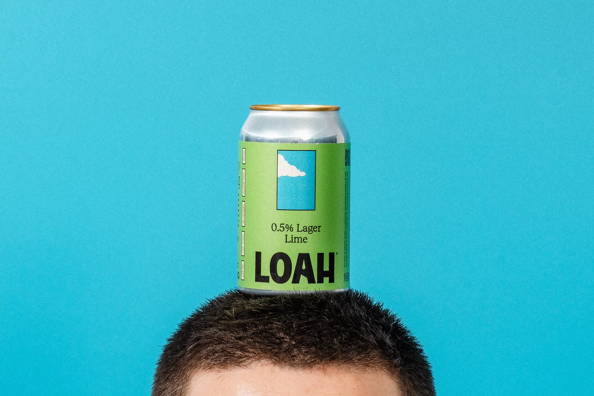 Overhead shot of lime flavored lager can balanced on an adult male's head against a bright blue background in a studio.