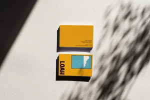 Two yellow Loah Beer Co. business cards arranged on a white textured background with soft leaf shadows.