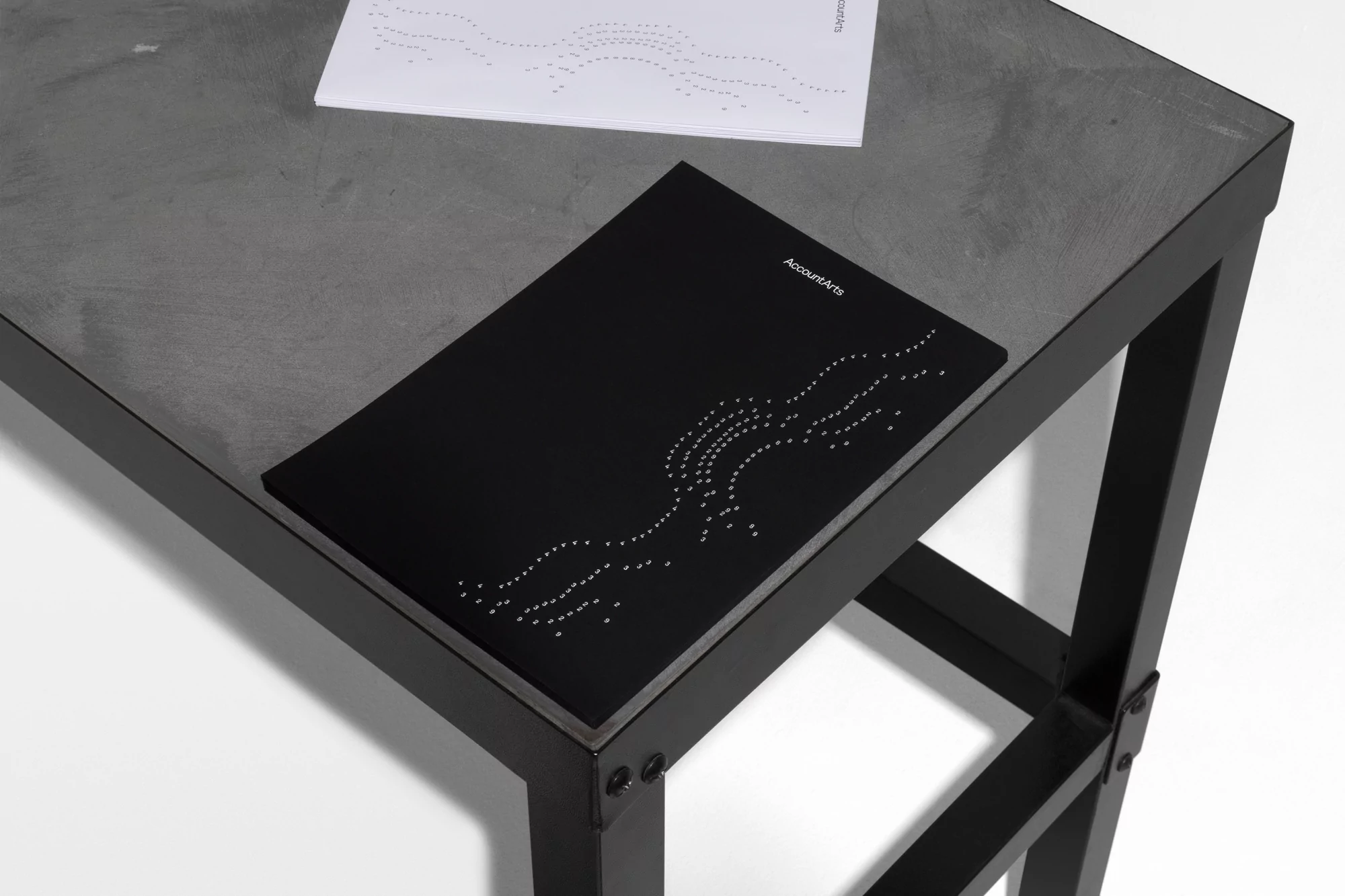 Black book with dotted line art on a dark grey table, next to a white booklet with similar dotted design, against a white background.