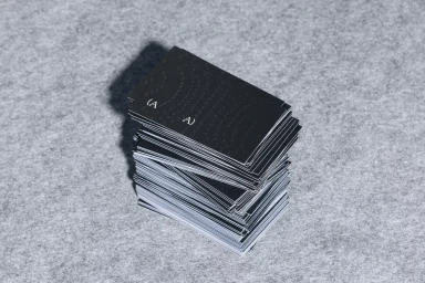 A stack of black business cards with subtle patterns resting on a grey textured surface.