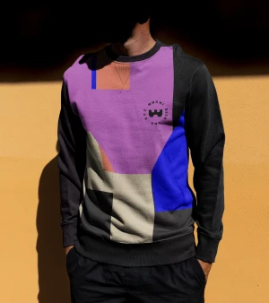 Man wearing a graphic print sweatshirt with purple and blue panels and dark trousers against a yellow wall