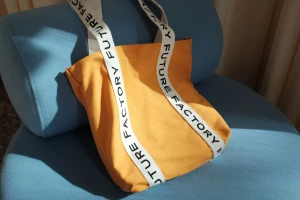 Mustard yellow canvas tote bag with white branded straps resting on a blue upholstered chair.