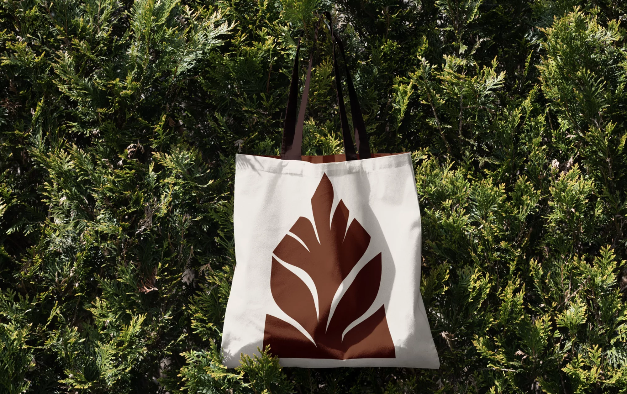 Tote bag with brown leaf design hanging against a green leafy background, showcasing eco-friendly style and nature-inspired design.