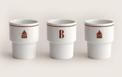 Three white ceramic stacking cups with brown trim and botanical letter graphics on a neutral background