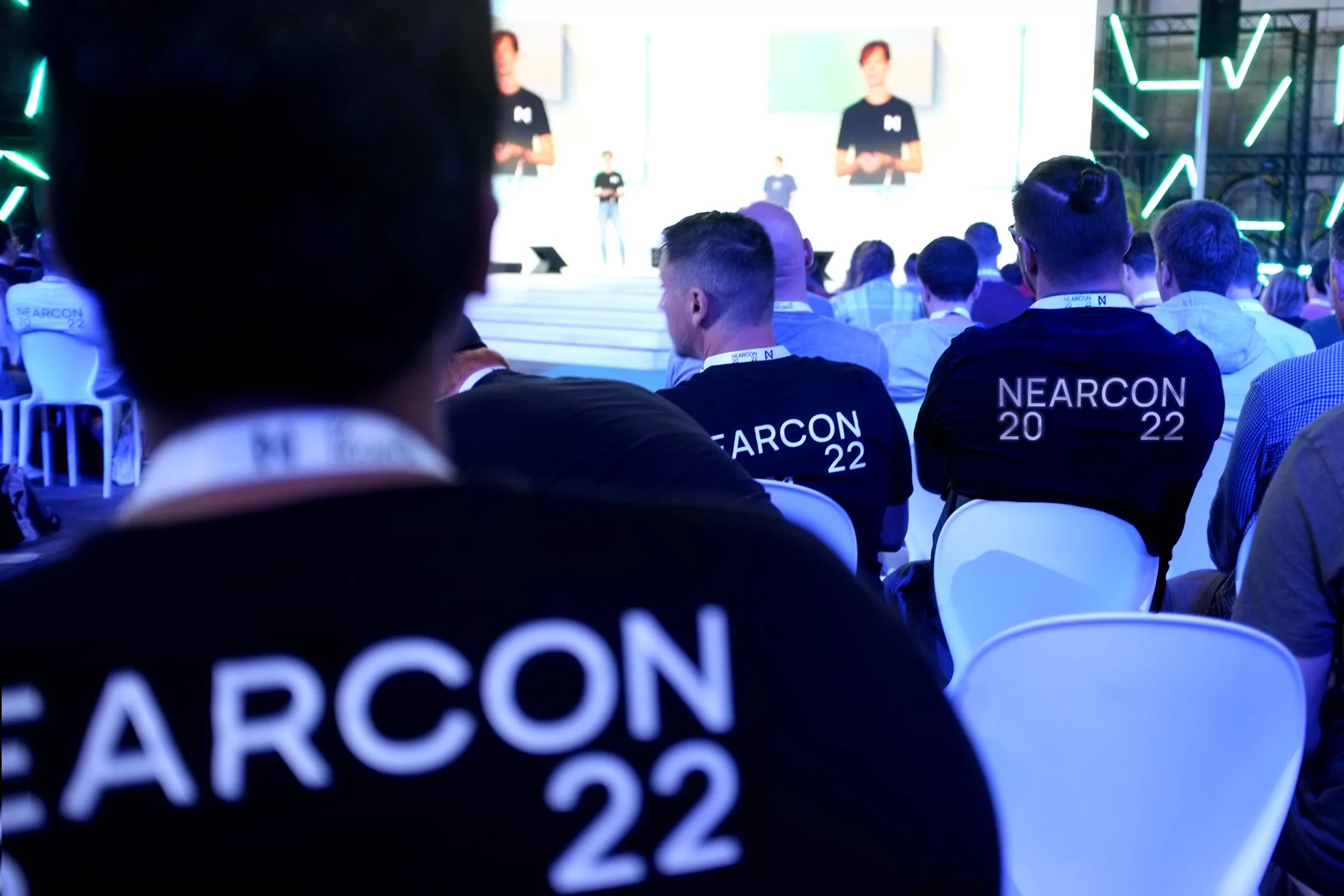 Audience at NEARCON 2022 event with a speaker on stage in the background. People wear matching shirts and identification around their necks.
