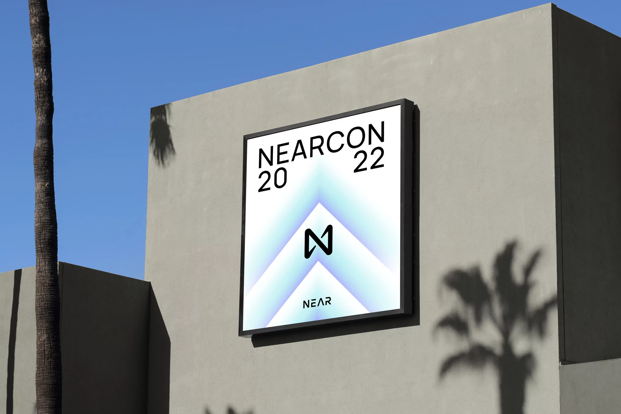 Outdoor advertising: a framed NEARCON 2022 poster attached to a gray wall next to a palm tree on a sunny day.