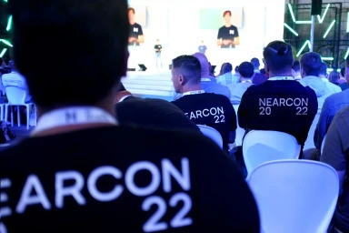 Audience members wearing black t-shirts with white NEARCON 22 text seated facing a conference stage.