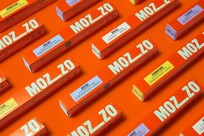 Arrangement of orange boxes of Mozzo coffee capsules with white text labels set against a matching orange background.