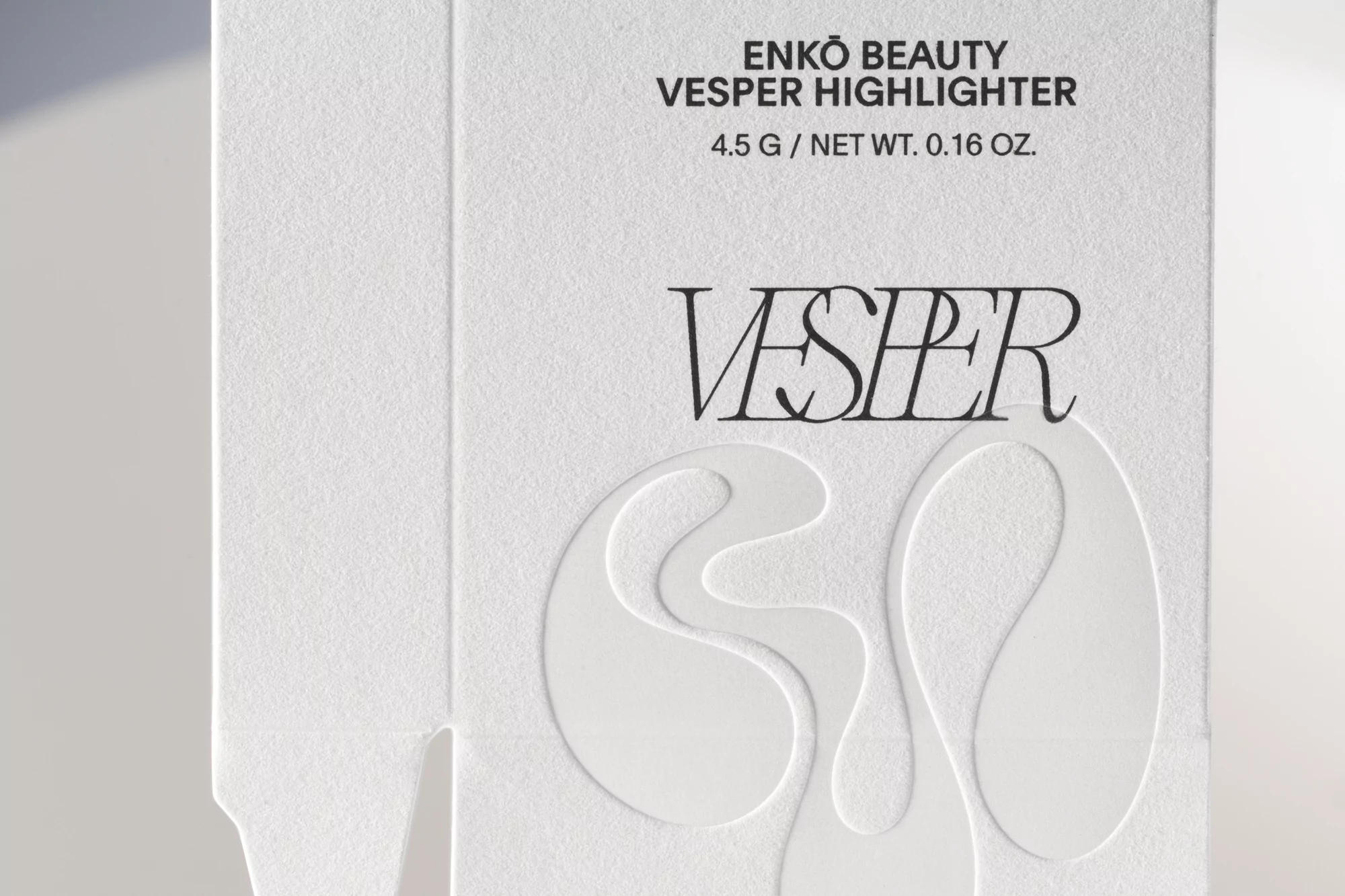 Close-up of white packaging for Enko Beauty Vesper Highlighter makeup, featuring embossed text and a modern, minimalist aesthetic.
