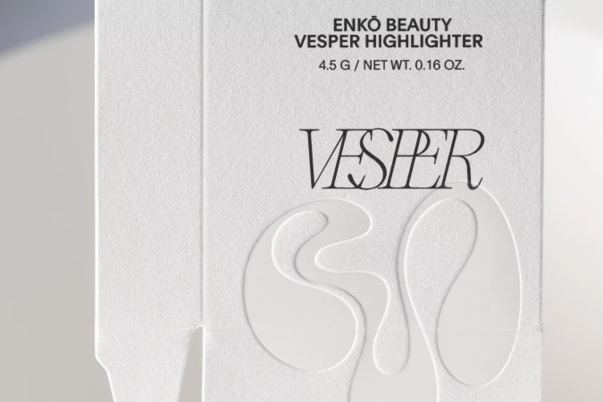 Close-up of white packaging for Enko Beauty Vesper Highlighter makeup, featuring embossed text and a modern, minimalist aesthetic.