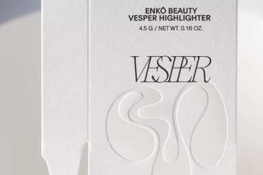 Close-up product packaging for EnKo Beauty Vesper Highlighter featuring embossed minimalist typography on textured white paper.