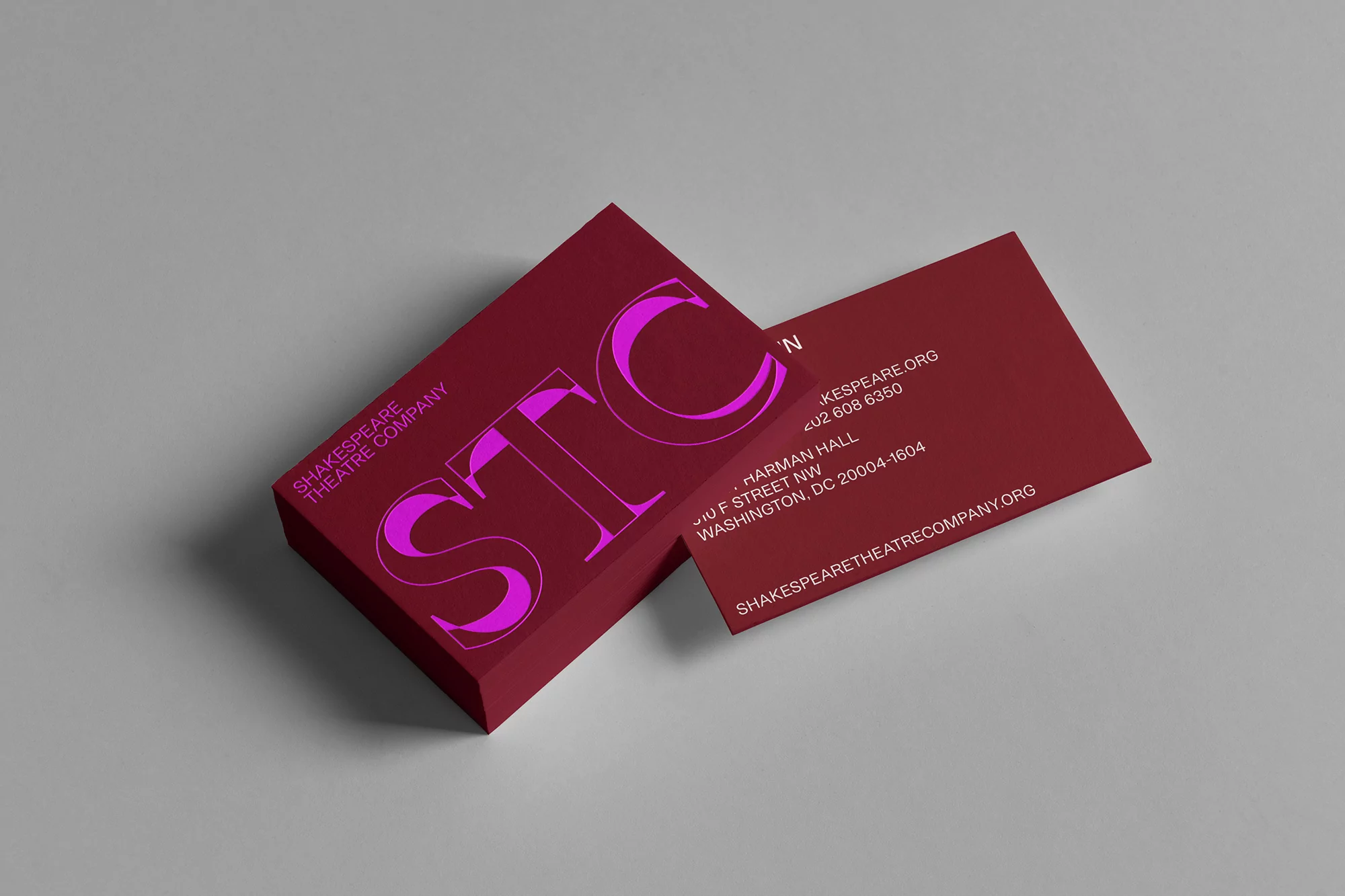 Stack of Shakespeare Theatre Company business cards in burgundy with pink letters and company information on a light gray background.