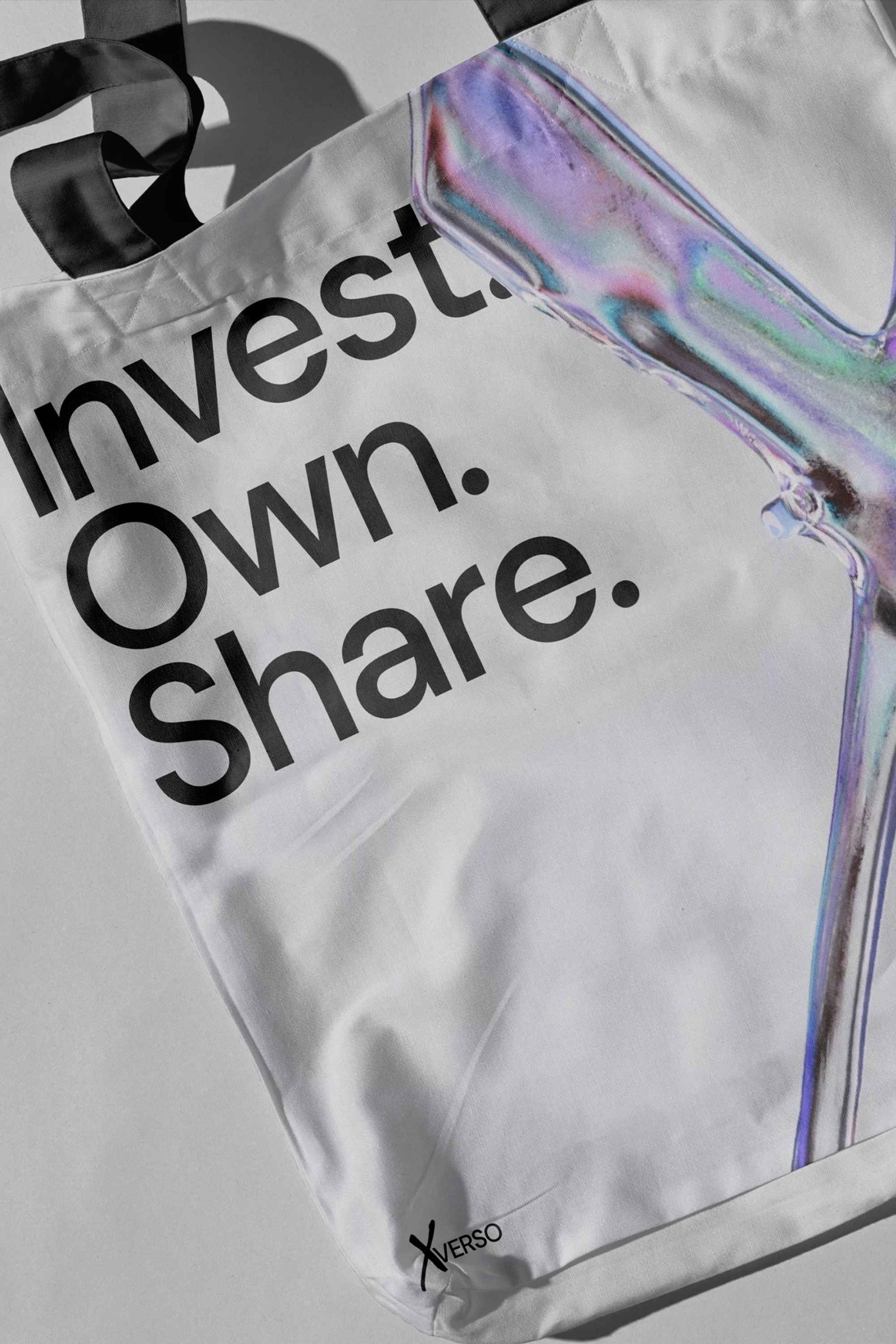 White tote bag with black handles, featuring the words 'Invest. Own. Share.' and an abstract design. Studio product shot.