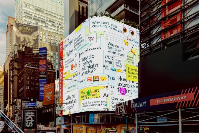 Urban scene featuring a building covered in text and emojis, surrounded by skyscrapers and billboards in a bustling city environment.