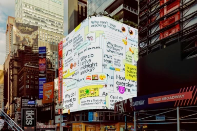 Giant digital billboard displaying typographic questions and emojis on a curved screen in a bustling urban street environment