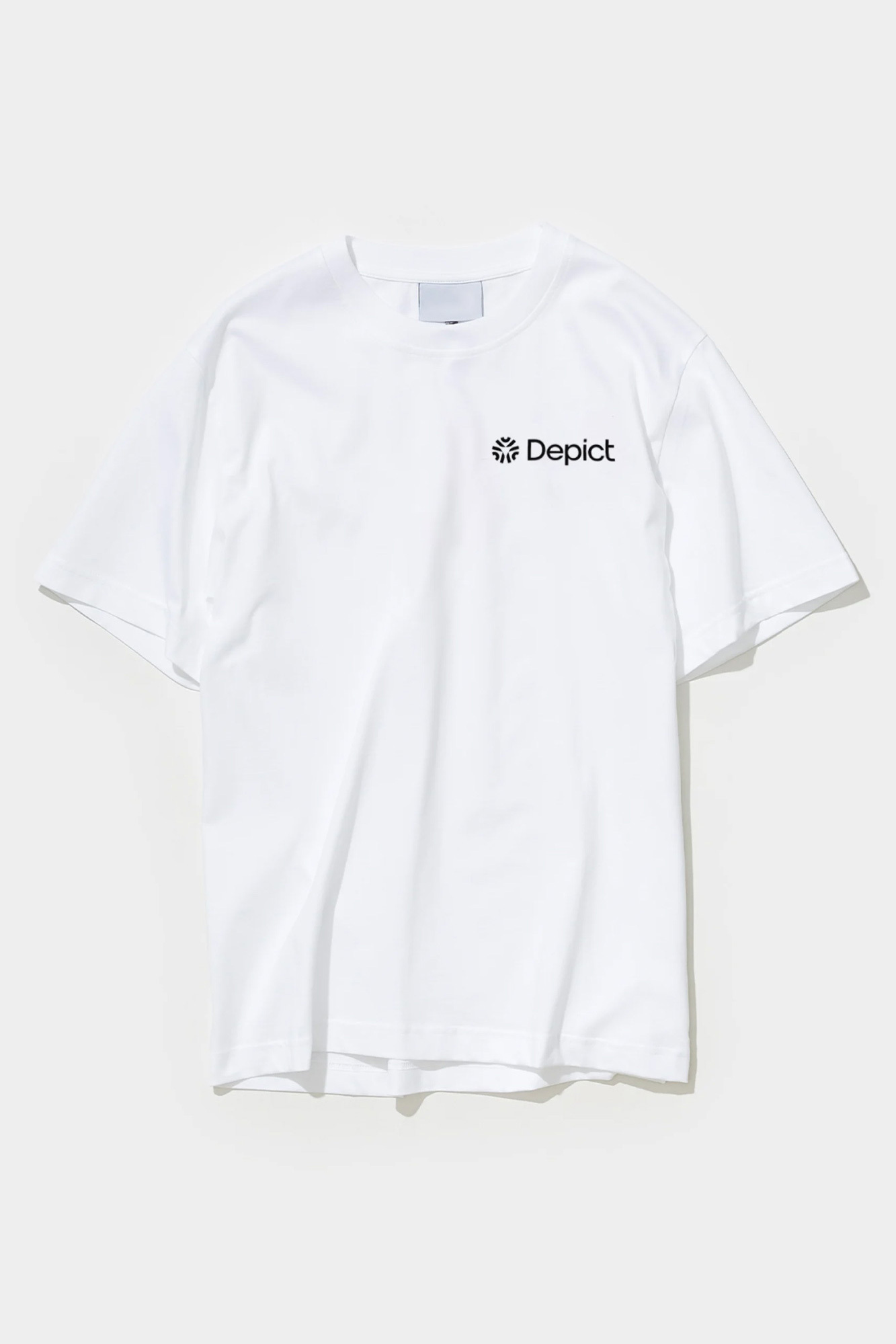 White t-shirt with the word 'Depict' on the upper right side of the shirt on a white seamless background in a studio setting.