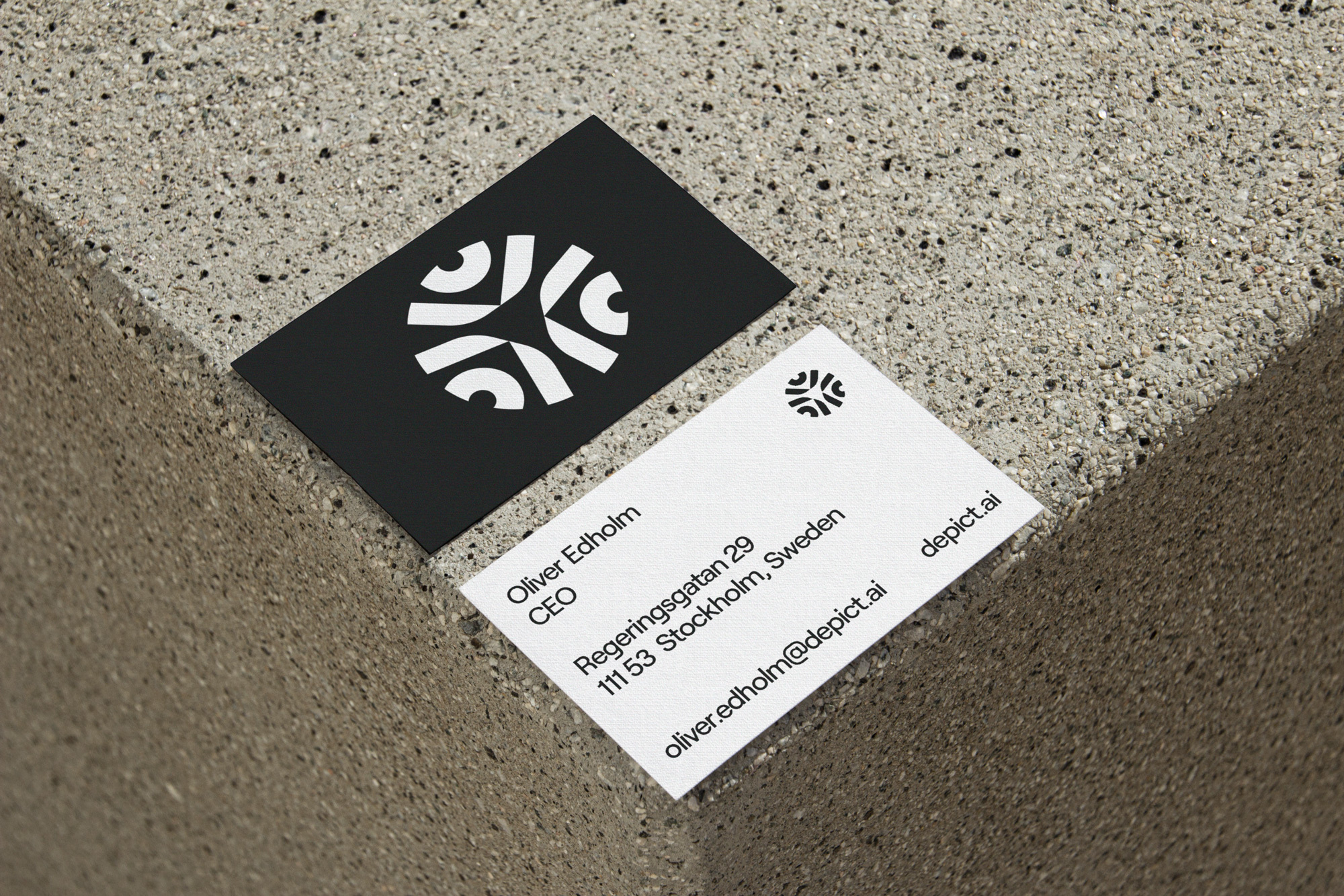 Close-up of two business cards, one black with a white logo, one white with contact information, resting on a concrete surface.