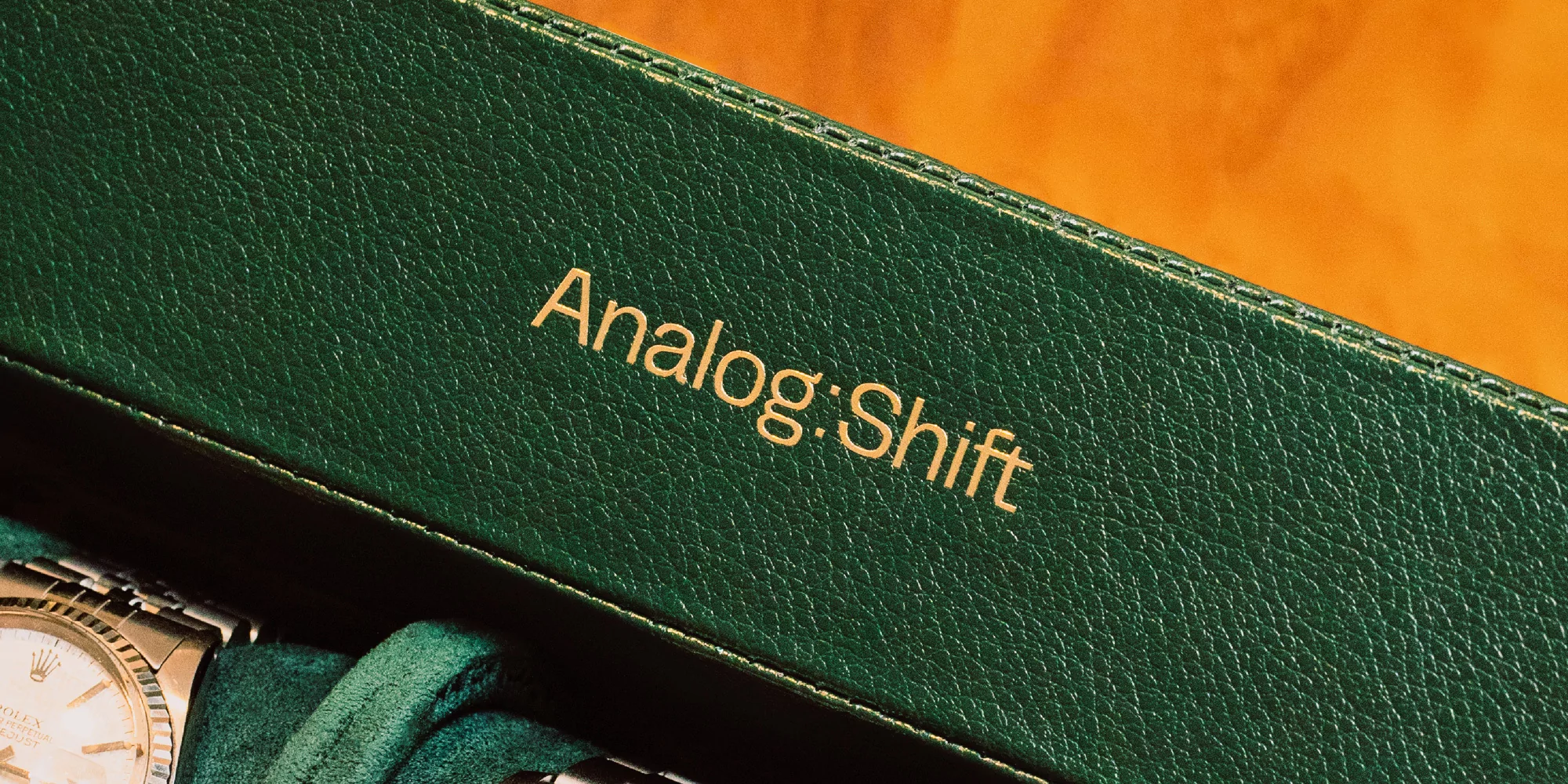 Close-up of a green textured box with 'Analog:Shift' in gold lettering, hinting at vintage watches and luxury accessories.
