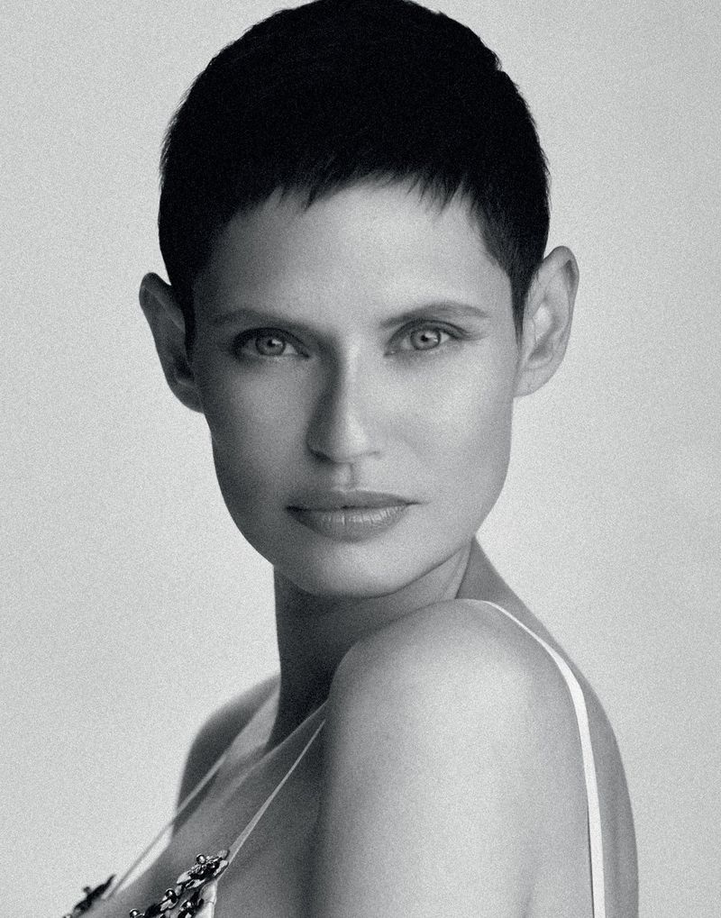 Monochrome portrait of a woman with a short, dark haircut and light eyes, wearing a light-colored top against a plain background.