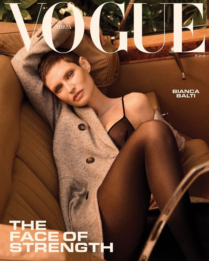 Vogue cover featuring model Bianca Balti in tweed jacket, black tights and bra, posing inside classic car with magazine text overlay.