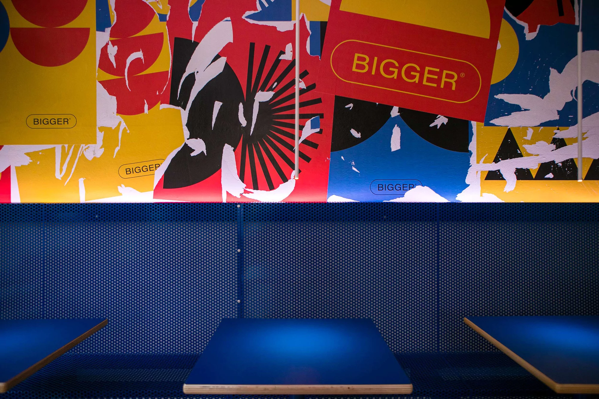 Close-up interior of a room with blue walls, featuring abstract red, yellow, and blue designs, and square tables on either side.