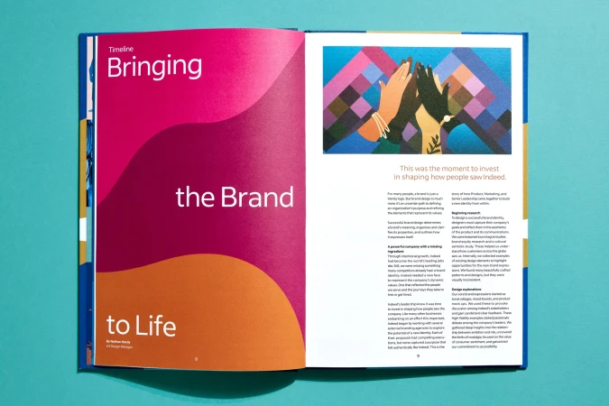 Open magazine spread on a blue surface featuring colorful graphics, text, and a geometric illustration of hands giving high-fives.