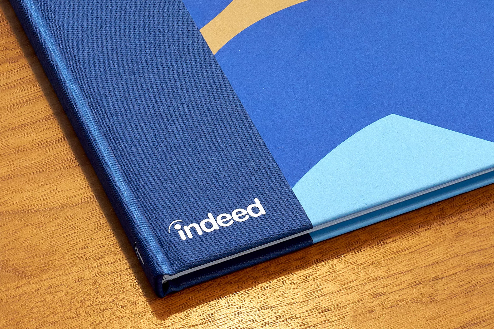Close-up on a blue book with the 'indeed' logo, showcasing graphic design and branding with a modern aesthetic on a wood surface.