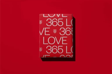 Red paper box with printed white 365 and LOVE typography set against a matching red background casting a soft shadow.