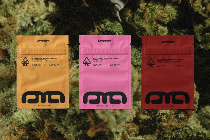 Three colorful MesoBis cannabis-infused gummies packages in yellow, pink, and red, displayed on a green cannabis background.
