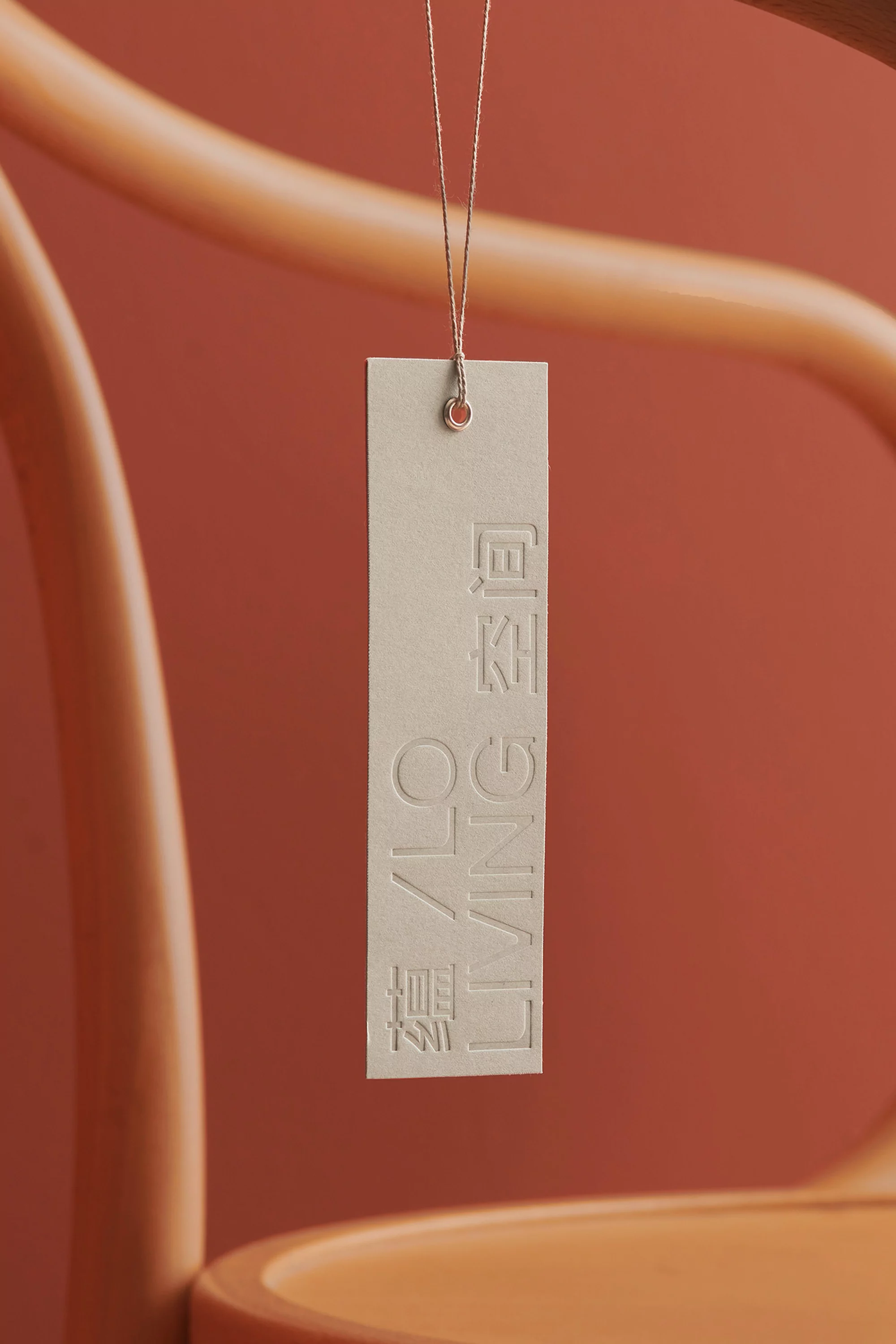 Product tag hanging from a light brown chair against a warm, reddish-brown background, featuring debossed text in Chinese and English.