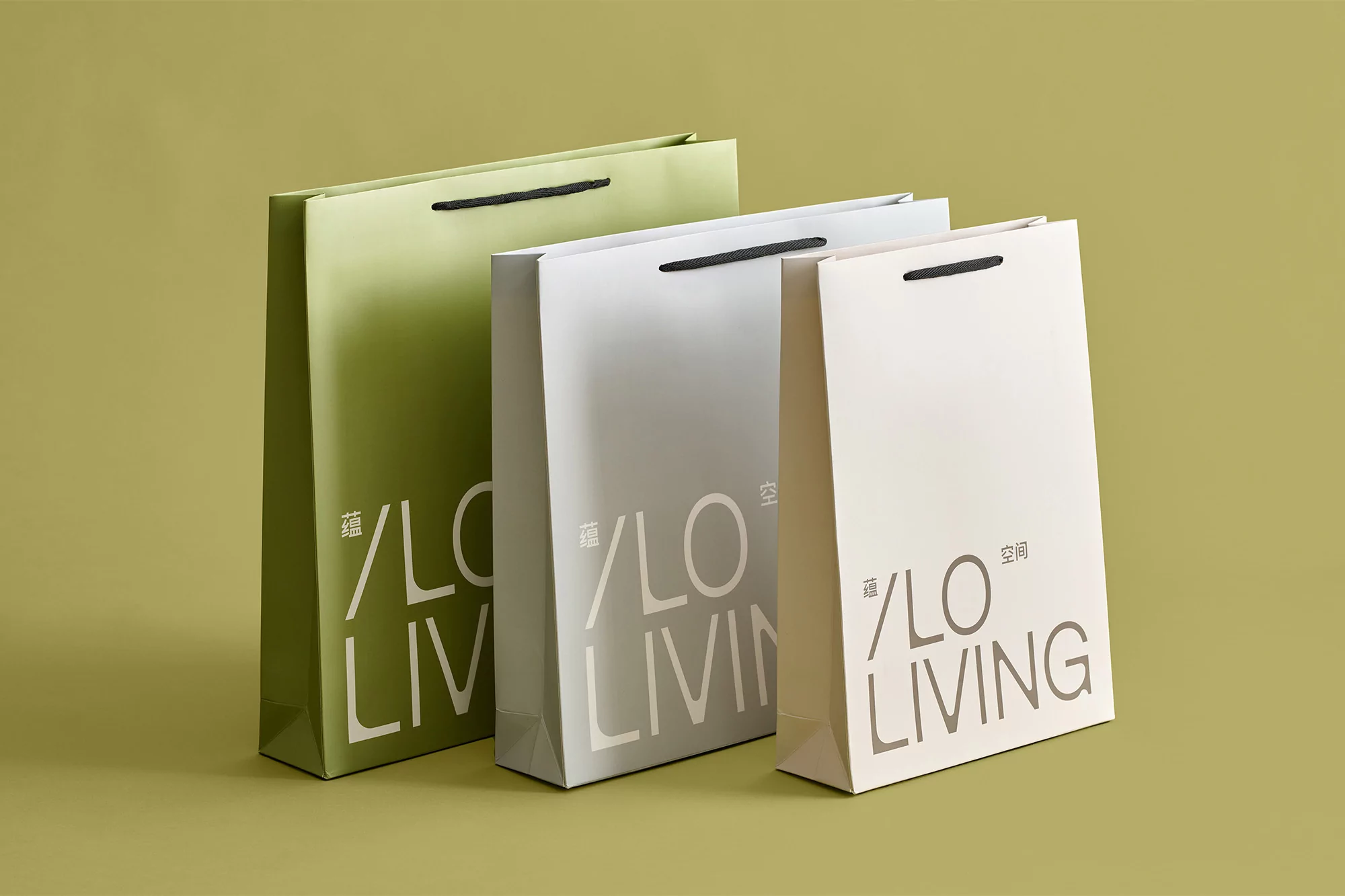Three paper shopping bags in green, gray, and light beige, feature a modern '/LO LIVING' logo, arranged against an olive green background.