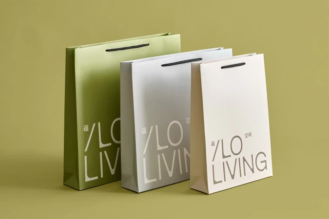 Three paper shopping bags in green, gray, and light beige, feature a modern '/LO LIVING' logo, arranged against an olive green background.
