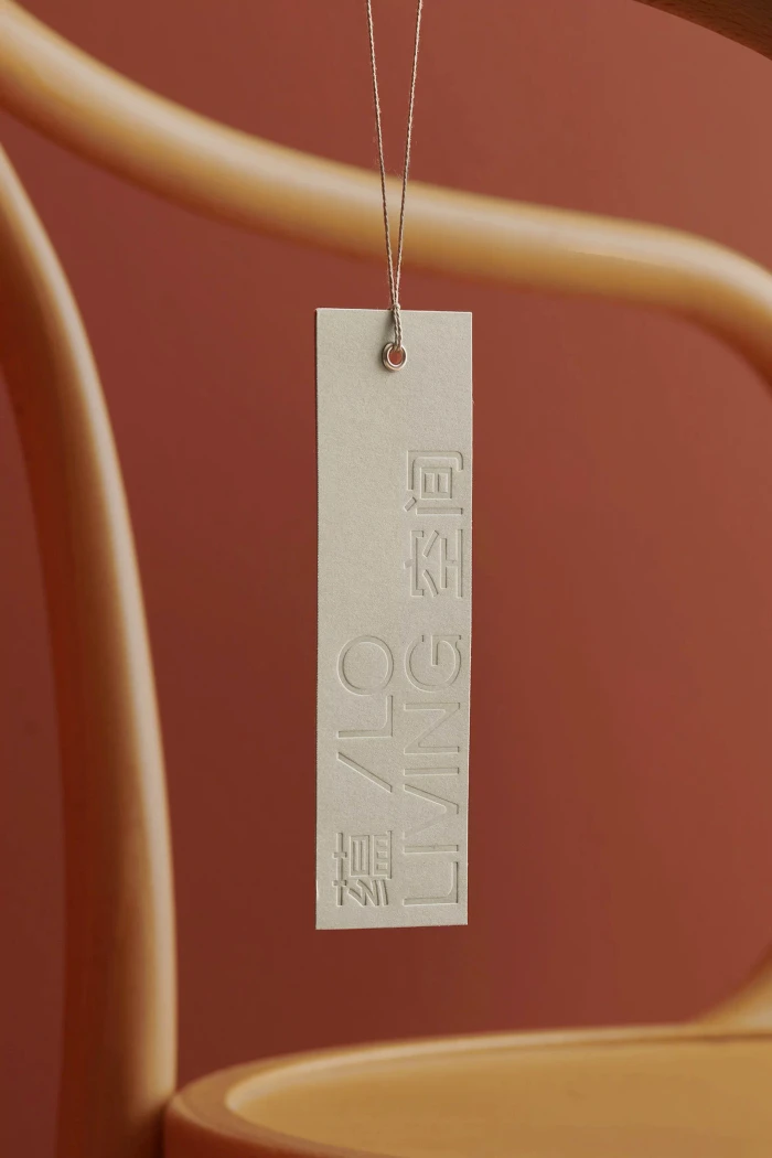 An off-white rectangular paper tag with embossed lettering hanging against a terracotta background and wooden chair