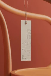 An off-white rectangular paper tag with embossed lettering hanging against a terracotta background and wooden chair