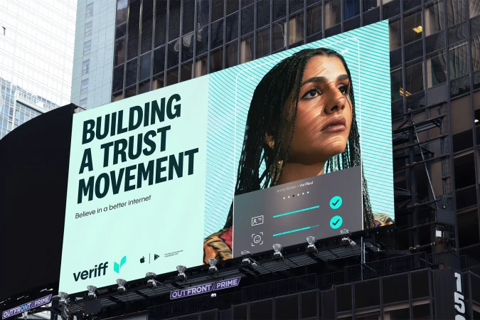 Woman's portrait on a billboard promoting Veriff, set against an urban backdrop with modern architecture and a teal and white color scheme.