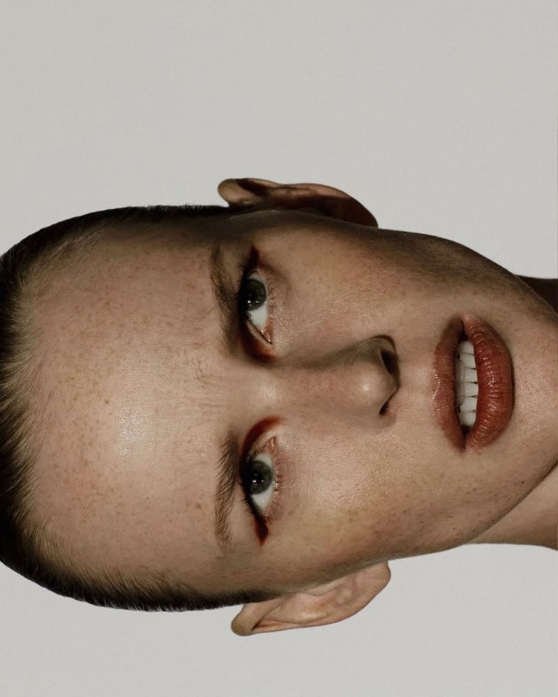 Close-up portrait of an adult female with green eyes and red lipstick, facing upward against a bright white background in a photo studio.