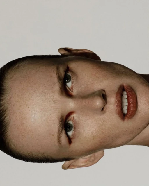 Close-up portrait of an adult female with green eyes and red lipstick, facing upward against a bright white background in a photo studio.