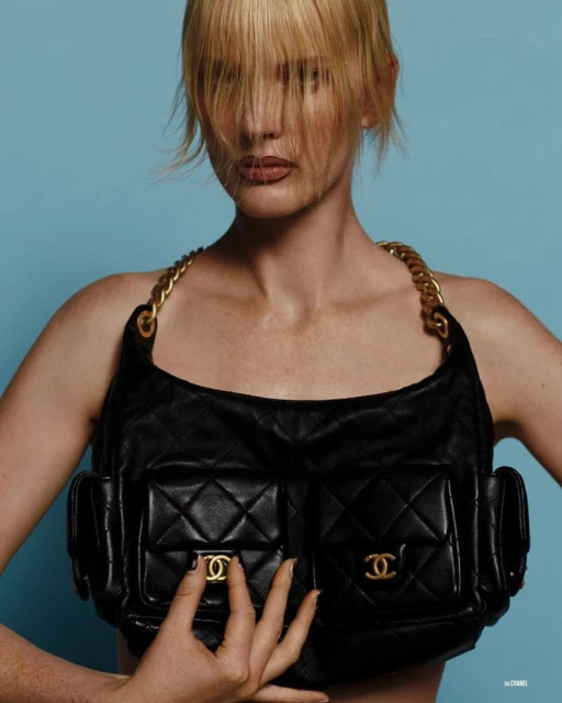 Woman with blond hair and a black Chanel bag with gold hardware against a light blue background, fashion shot, studio lighting.