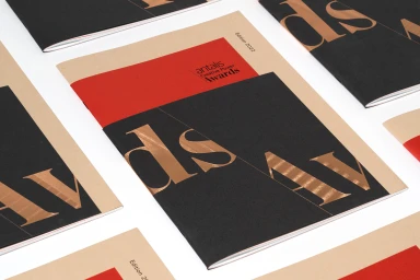 Multiple brochures featuring a red, black, and tan cover design with metallic typography displayed on a white surface.