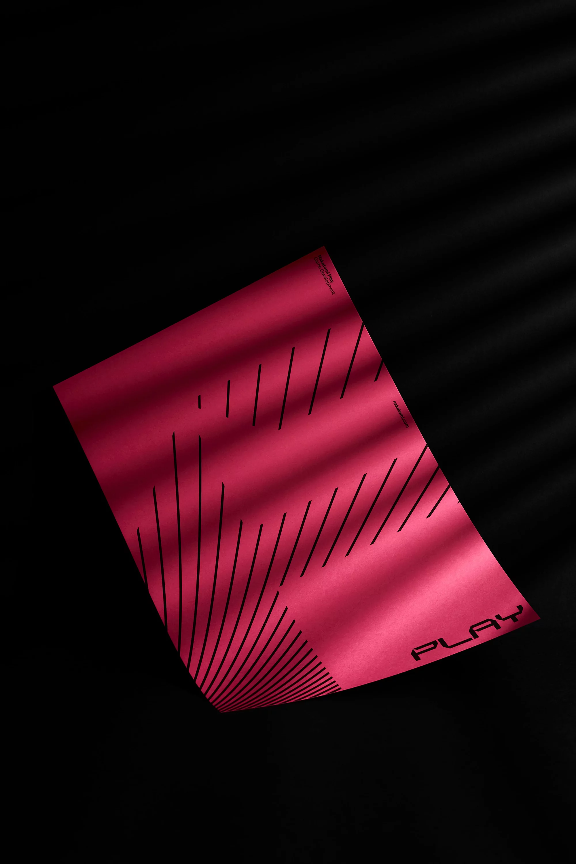 Abstract studio shot of pink paper with black lines and the word 'PLAY' against a dark background with shadow patterns.