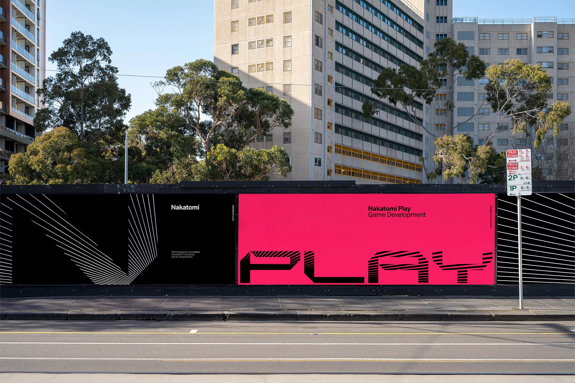 Outdoor advertising billboard featuring 'Nakatomi Play Game Development' in black and pink on a city street with buildings and trees.