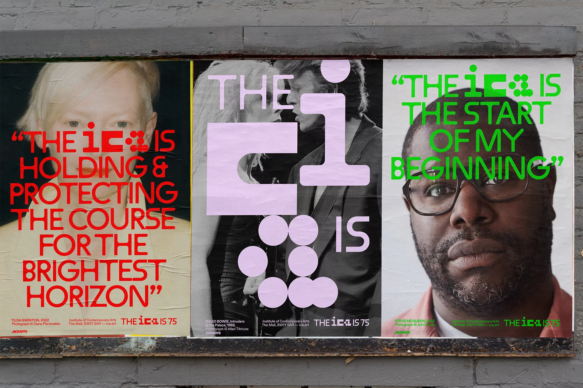 Eye-level shot of three artistic posters attached to a wall, featuring portraiture, vibrant text, and abstract designs in an urban environment.